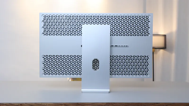 Geperforeerde achterkant van de Kuycon G32P-monitor op een bureau, met zijn zilverkleurige voet en de rij aansluitingen